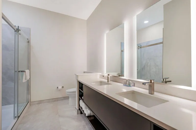 Bathroom with double vanity, lit mirrors and a glass walk-in shower