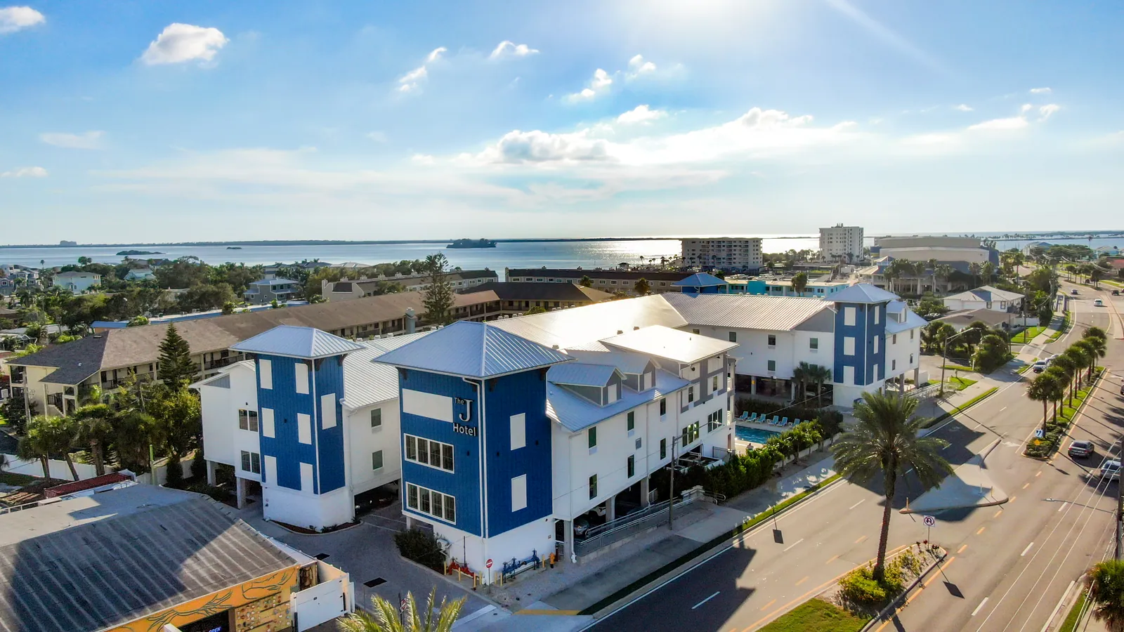 Aerial view of The J Hotel's blue towers and white buildings on Causeway Boulevard, with the water behind