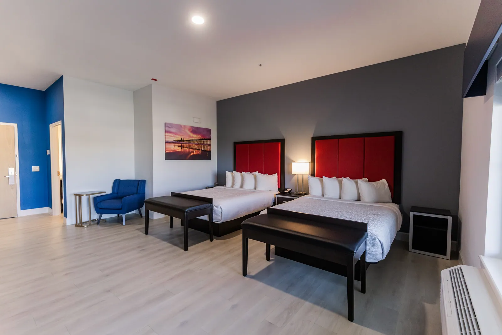 Two queen room with red headboards, a blue armchair and wood floors
