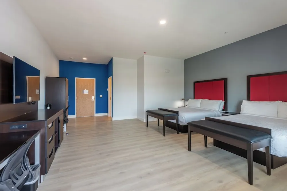 Large guest room with two queen beds, blue accent wall and red headboards